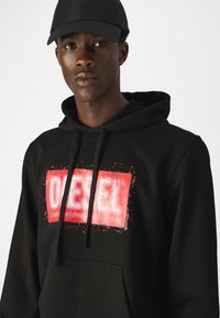 Black hoodie with a textured, printed red rectangular logo reading "DIESEL." Features a kangaroo pocket and drawstring hood.