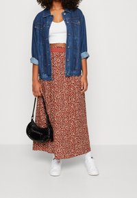 Jeansjacke, weißes Croptop, floraler Maxikleid in Rost mit weißen Akzenten und schwarze Handtasche. Weiße Sneaker runden das Outfit ab.