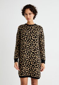 Knit suknelė su leopardų raštu juoda ir tan spalvomis. Ilgos rankovės, apvalus iškirpimas, ir pynimo rankogaliai bei apatinė dalis. Minkšta tekstūra.