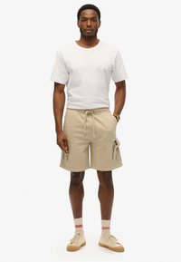 Pantaloni cargo beige con due tasche laterali, cintura elastica e cordoncino. Abbinati a una t-shirt bianca semplice e sneaker color sabbia.