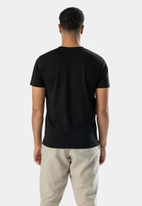 Sort kortærmet T-shirt med rund hals, glat tekstur, tætsiddende design, set fra ryggen, sammen med lysfarvede bukser.