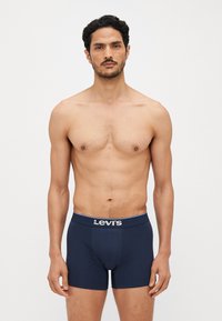 Sötétkék boxeralsó, puha tapintással, kontrasztos szürke derékpánttal, amelyen a "Levi's" felirat található. A modell póló nélkül, előrefordulva áll.
