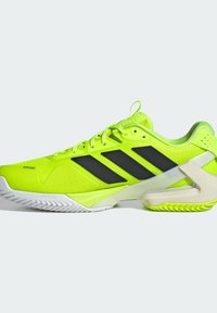 Baskets de sport jaune fluo avec des rayures noires, une tige texturée et une semelle blanche avec un motif en zigzag. Le design comprend un talon renforcé.