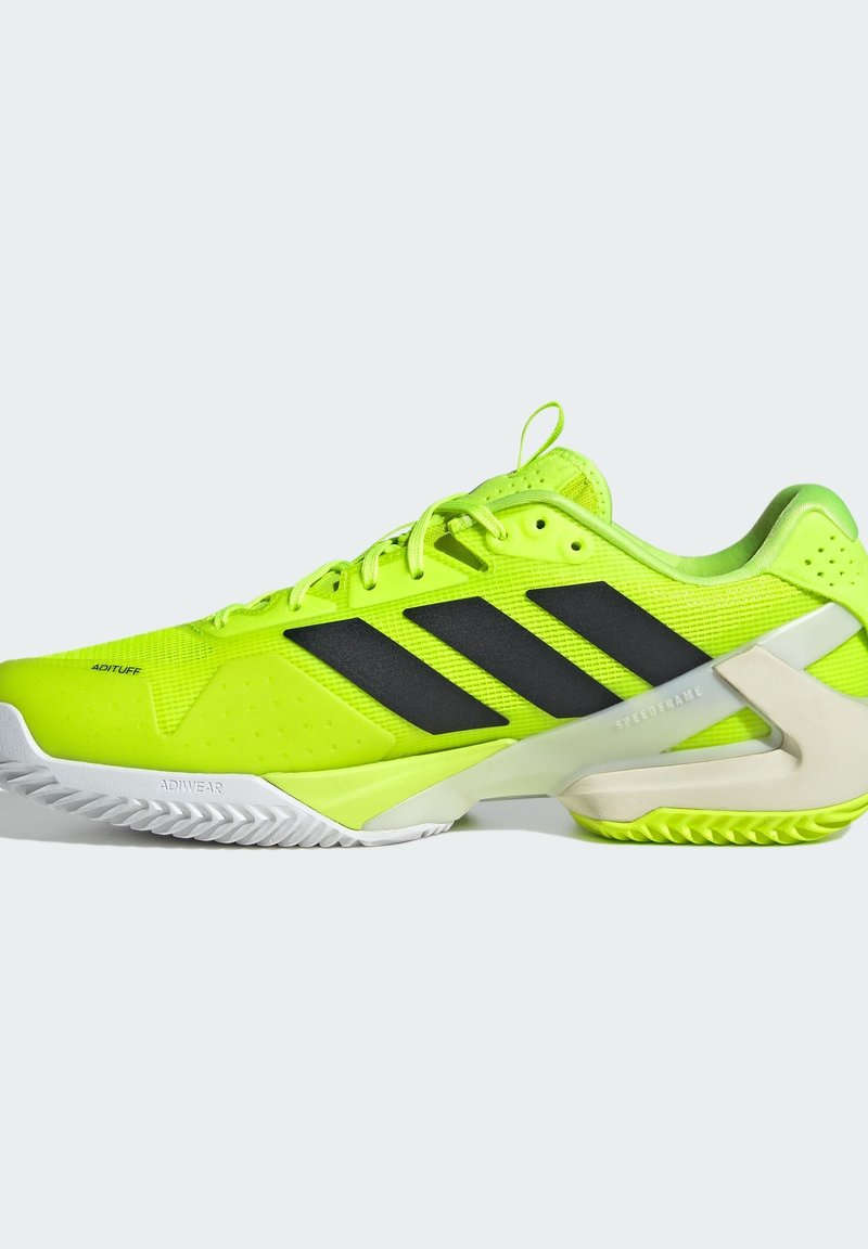 Baskets de sport jaune fluo avec des rayures noires, une tige texturée et une semelle blanche avec un motif en zigzag. Le design comprend un talon renforcé.