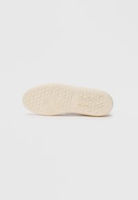 Sko såle med sirkulære og lineære mønstre i beige gummi, isolert på en hvit bakgrunn, som viser grepdesign.