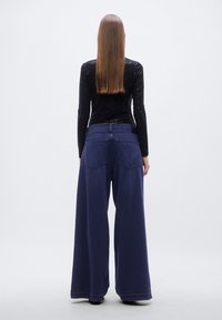 Φαρδιά παντελόνια σε βαθύ ναυτικό μπλε, κατασκευασμένα από απαλό ύφασμα. Διαθέτουν δύο πίσω τσέπες και μέση μεσαίου ύψους, συνδυασμένα με εφαρμοστή μαύρη μπλούζα.