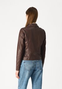 Brun skinnjakke med en tettsittende design, som har krage, lange ermer og sømdetaljer, satt sammen med lyseblå denimjeans.
