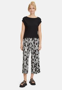 Schwarzes kurzärmliges Oberteil kombiniert mit weit geschnittenen Hosen mit weißem Blumenmuster. Schwarze Sandalen runden das Outfit ab.