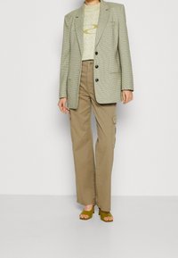 Kostkovaný zelený blazer přes světlý žlutý grafický tričko, spárovaný s khaki cargo kalhotami; obsahuje široké nohavice a olivově zelené sandály na podpatku.