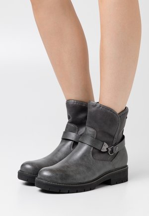 Grå läderstövletter med uppvikbar mudd och en detaljerad rem med silverfärgad metall. Robust gummisula för hållbarhet.