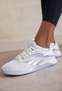 Light gray athletic shoe with a breathable fabric upper, white and pastel blue accents, lace closure, and textured sole for traction.