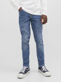 Jeans de ganga azul com um corte slim, apresentando cinco bolsos e uma textura de lavagem subtil. Acompanhados por ténis azul-marinho com atacadores brancos.