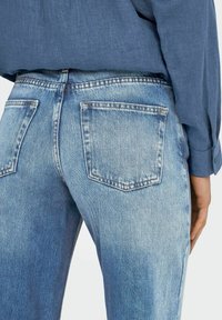 Světle modré džíny z denimu s vybledlým vzhledem, vybavené dvěma zadními kapsami. Textura je hladká, s rovnými nohavicemi a minimálními detaily šití.