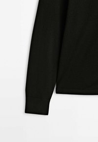 Manche longue noire d'un pull en tricot avec poignets et ourlet côtelés sur fond blanc.