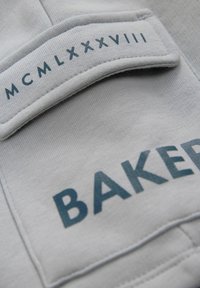 Hall gray kangas, millel on sile tekstuur, ja millel on ristkülikukujuline silt tumeda sinise tekstiga, millel on kirjas "BAKER" ja rooma numbrid "MCMLXXXVIII" selle üle.
