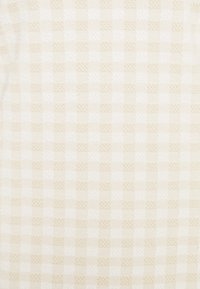 Tejido texturizado en un tono beige claro con un sutil patrón a cuadros. Los cuadrados alternan entre tejidos lisos y ligeramente texturizados.