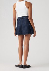 Jeansowa spódnica typu skater w ciemnoniebieskim kolorze z dopasowanym stanem i rozszerzanym dołem. Noszona z białym podkoszulkiem w prążki i czarnymi płaskimi butami.