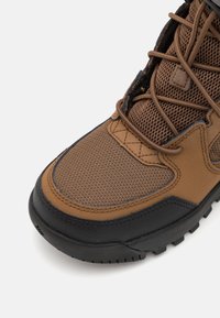 Brauner Wanderschuh aus Mesh- und Synthetikmaterialien, mit runder Zehenpartie, kontrastierender schwarzer Gummisohle und kunstvollen Schnürdetails.