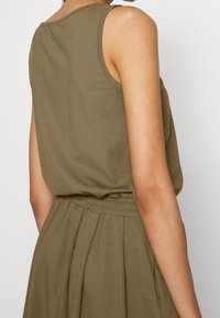 Oliwkowy, bezrękawnik o luźnym kroju, z okrągłym dekoltem i plisowaniami w talii. Miękka, gładka faktura materiału.