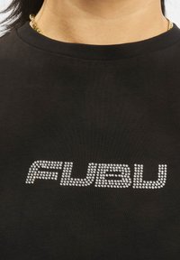 Čierne tričko s krátkym rukávom s logom "FUBU" z kamienkov, okrúhlym výstrihom a jemnou bavlnenou textúrou.