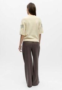 Pull crème à manches courtes avec des accents brodés sur les manches, associé à un pantalon large et ample de couleur brun foncé. Design et coupe simples.