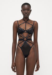 Lingerie nera in tessuto trasparente con un motivo a zigzag. Strutturata con spalline e borchie metalliche. Il design complessivo esalta la forma del corpo.