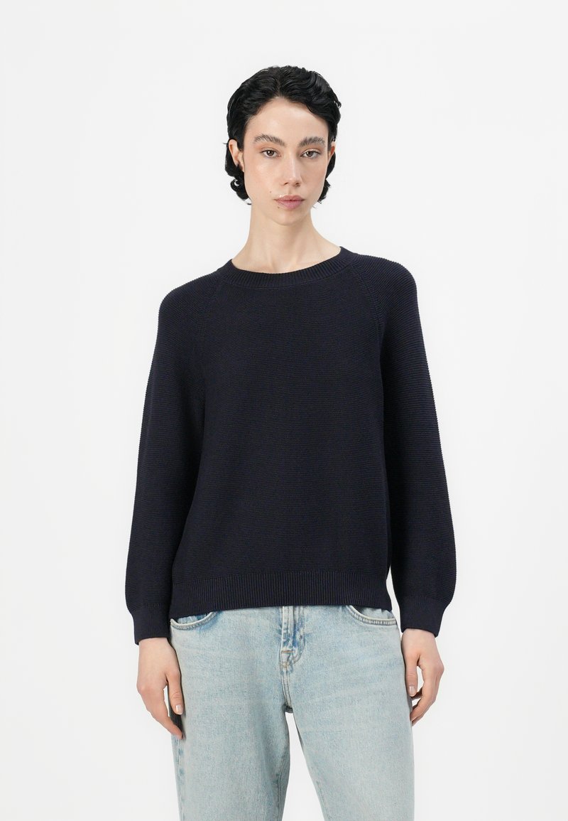 Ναυτικό πλεκτό πουλόβερ με στρογγυλή λαιμόκοψη, μακρ�ιά μανίκια και ριχτό τελείωμα, συνδυασμένο με ανοιχτό μπλε τζιν σε χαλαρή εφαρμογή.