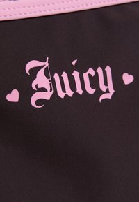 Tissu noir avec bordure rose cousue et le mot « Juicy » en police anglaise ancienne rose, flanqué de deux formes de cœurs roses.