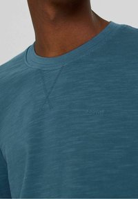 Camiseta corta de manga azul, hecha de una tela suave y texturizada. Presenta un escote redondo y un sutil detalle del logo en la parte frontal.