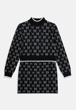 Crni pleteni pulover s bijelim uzorkom. Ima visoki ovratnik i rebraste manšete, što stvara prilagođeni siluetu.