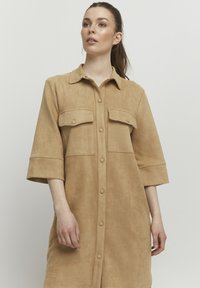 Béžové košilové šaty z imitace suede s límečkem, dvěma předními kapsami a zapínáním na knoflíky, s tříčtvrtečními rukávy a měkkou texturou.