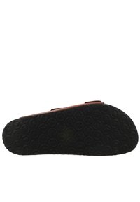 Piros slip-on cipő, két állítható pánttal, fekete gumitalppal, amelyen körkörös minták találhatók, valamint szilárd oldalakkal.