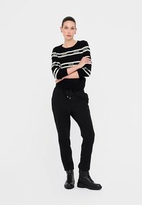 Sweter w czarno-białe paski z akcentami z logo, z okrągłym dekoltem i rękawami do łokcia, zestawiony z czarnymi, zwężanymi spodniami i botkami na kostkę.
