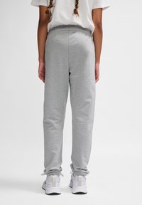 Graue Sweatpants mit einem elastischen Bund und geschnittenen Knöcheln, aus weichem Stoff, kombiniert mit weißen Sportschuhen.