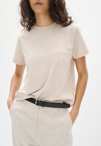 Beige T-shirt met korte mouwen, gemaakt van zachte stof, met een ronde hals. Gecombineerd met lichte linnen broek en een zwarte leren riem.