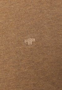 Brauner strickstoff mit einem subtilen strukturierten Muster und einem kleinen, geprägten Logo in der unteren Mitte. Glatte Oberfläche und mittlere Dicke.
