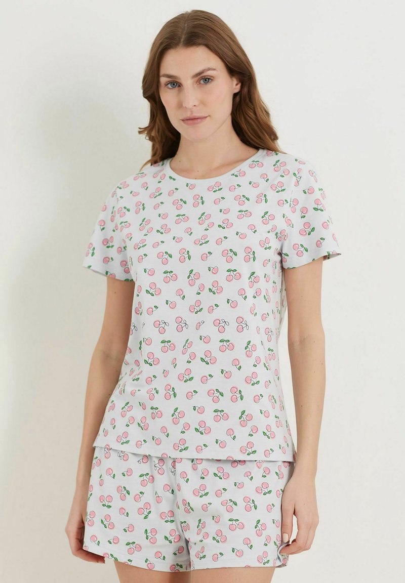 Vaaleanpunaiset pyjamat, joissa on hedelmäpainatus kirsikoista ja lehdistä, valmistettu pehmeästä puuvillakankaasta. Paitana on lyhythihainen yläosa ja sitä täydentävät shortsit.