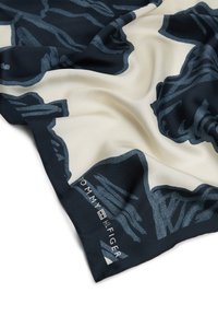 Pañuelo de seda con base crema, con un diseño abstracto en azul marino. Incluye un logo de "Tommy Hilfiger" en azul, ubicado en una esquina. Textura suave.