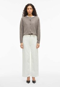 Cárdigan de punto gris con cuello redondo y botones, combinado con unos pantalones vaqueros anchos de talle alto en blanco y zapatos negros de punta.