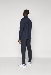 Navy long-sleeve top with a high collar paired with gray tapered pants and white sneakers. Smooth fabric texture, no visible patterns.