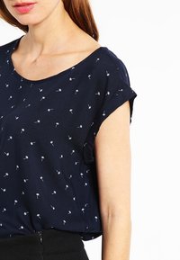 Tummansininen paita, jossa on lyhyet käännetyt hihat ja valkoinen kukkakuosi. Kevyestä kankaasta valmistettu, siinä on rento malli ja pyöreä kaula-aukko.