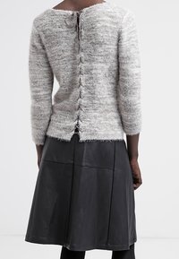 Szary sweter z teksturowanym splotem, z rękawami 3/4 i detalami zapięcia z tyłu, zestawiony z czarną skórzaną spódnicą o panelowym fasonie.