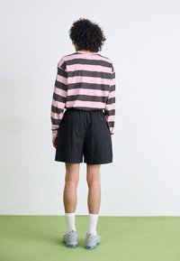 Long-sleeve pink and dark gray striped shirt, black shorts, gray sneakers, white socks, against a plain background with green flooring.