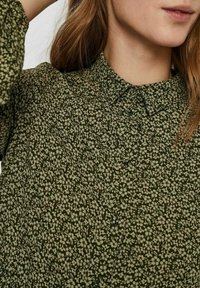 Blusa floreale verde con colletto, realizzata in un tessuto testurizzato, con piccoli motivi di fiori bianchi e chiusura con bottoni sul davanti.