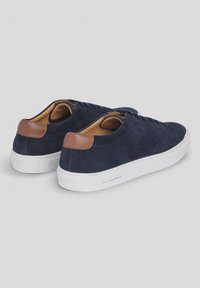 Granatowe zamszowe trampki z brązowymi skórzanymi akcentami na pięcie, białą gumową podeszwą i sznurowanym designem. Charakteryzują się gładką teksturą i minimalistycznym stylem.
