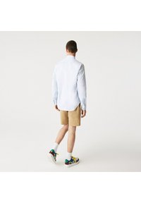 Light blue long-sleeve shirt, beige shorts, white socks, colorful sneakers. Shirt features a collar and side slits; shorts have a casual fit.