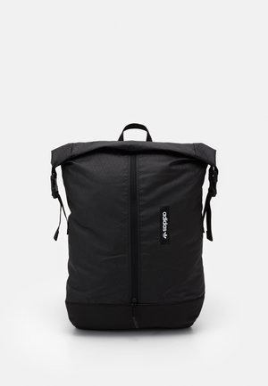 Sac à dos noir Adidas à ouverture roulante, avec fermeture éclair avant, boucles latérales et poignée supérieure sur fond blanc uni.