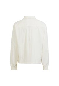 Bílá bunda s límcem, elastickými manžetami a mírně volným střihem. Na levém rukávu je výšivka. Jednoduchý zadní pohled.