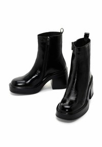 Bottes noires brillantes à cheville avec talons carrés épais, fermetures éclair latérales et languettes à l'arrière, présentées sur un fond blanc.