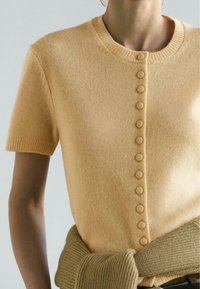 Short-sleeve, round-neck knit top in soft yellow with textured fabric, featuring button detailing along the front and a ribbed collar.